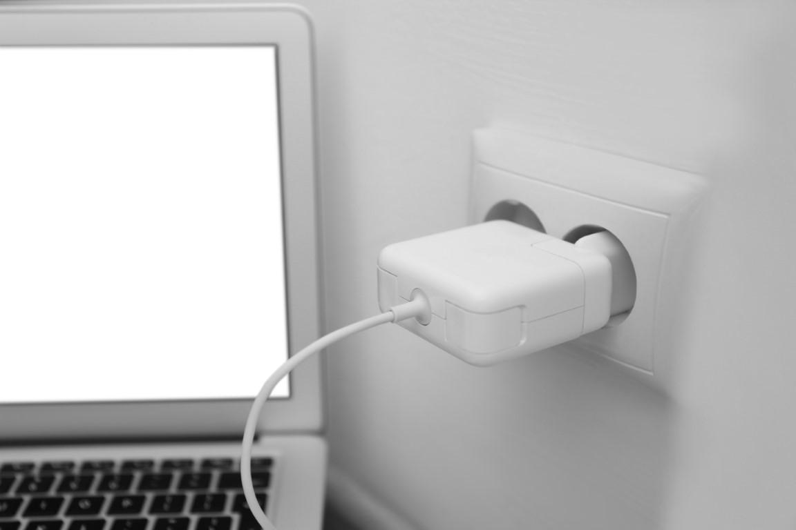 Modern laptop charging from electric socket indoors, closeup